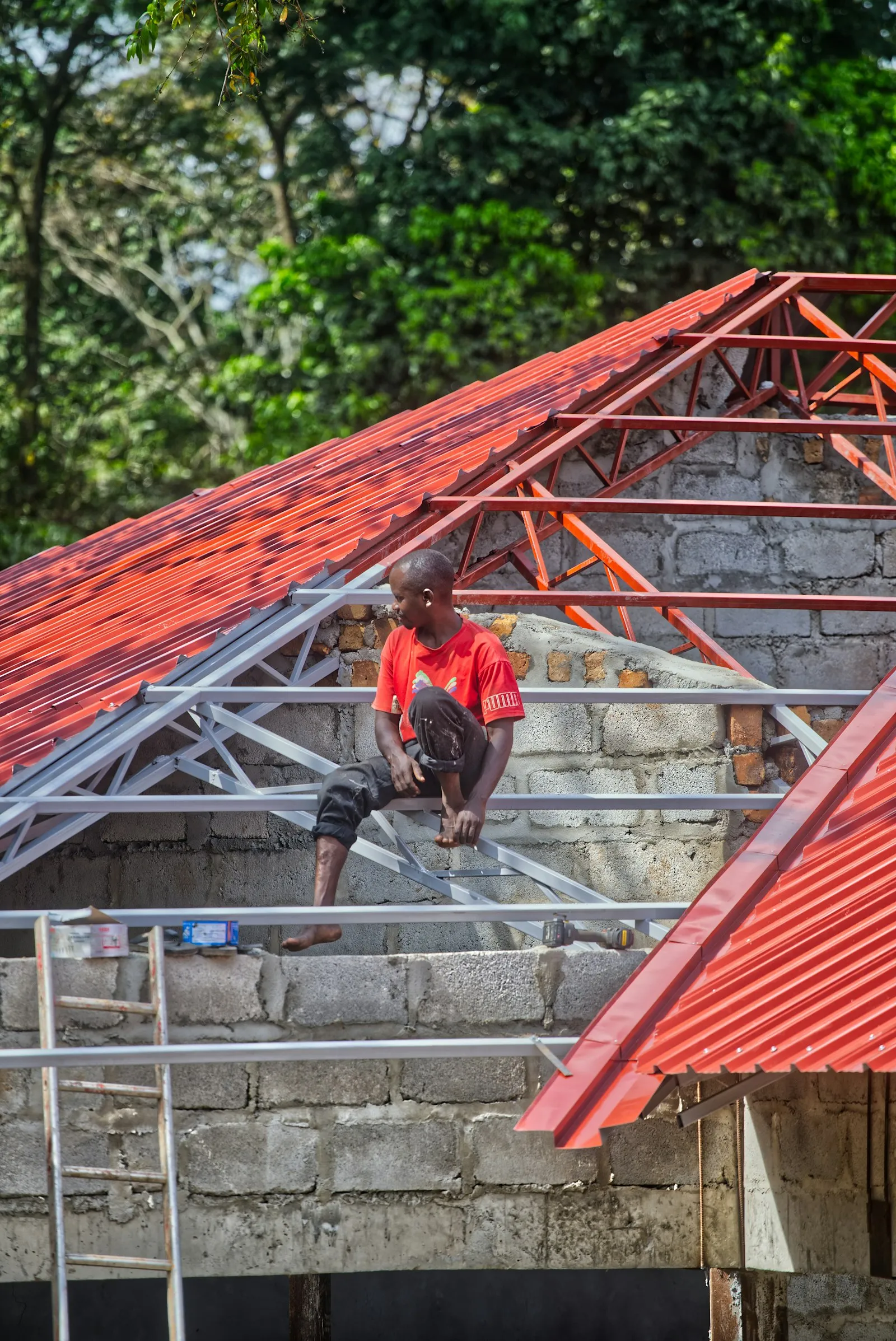 Pekerja memasang genteng metal merah baru pada rangka atap di Bekasi Selatan